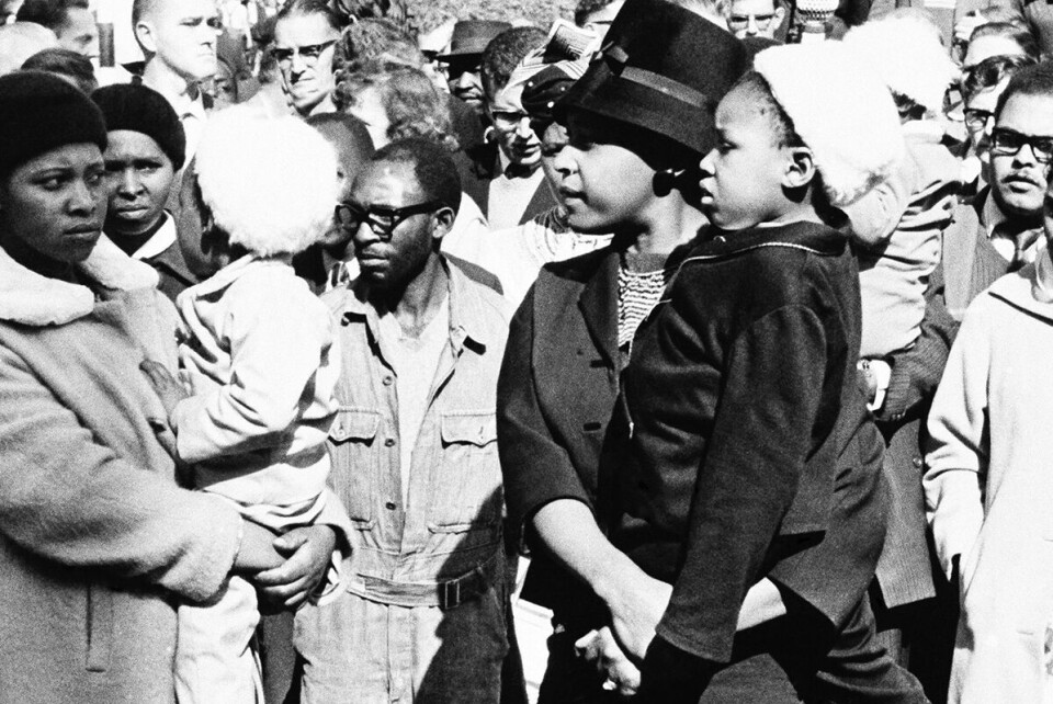 Winne Mandela (i svart) med sin datter på armen utenfor rettslokalet i Pretoria i 1964 der de håpet å få en glimt av Nelson Mandela som sto tiltalt for høyforræderi.