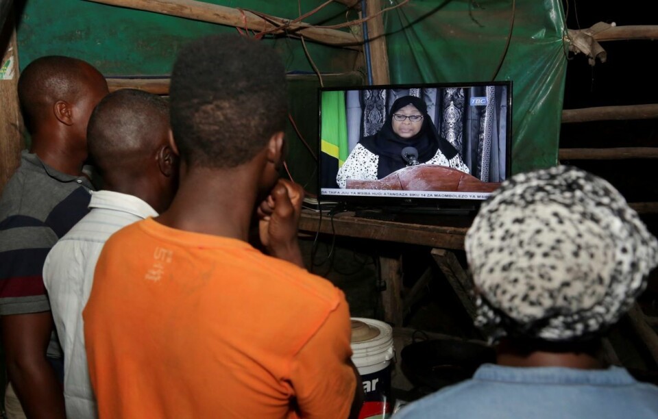 Folk i Dar es Salaam følger med nyhetssendingen der visepresident Samia Suluhu Hassan informerer om at presidenten er død. Foto: Emmanuel Herman / Reuters / NTB