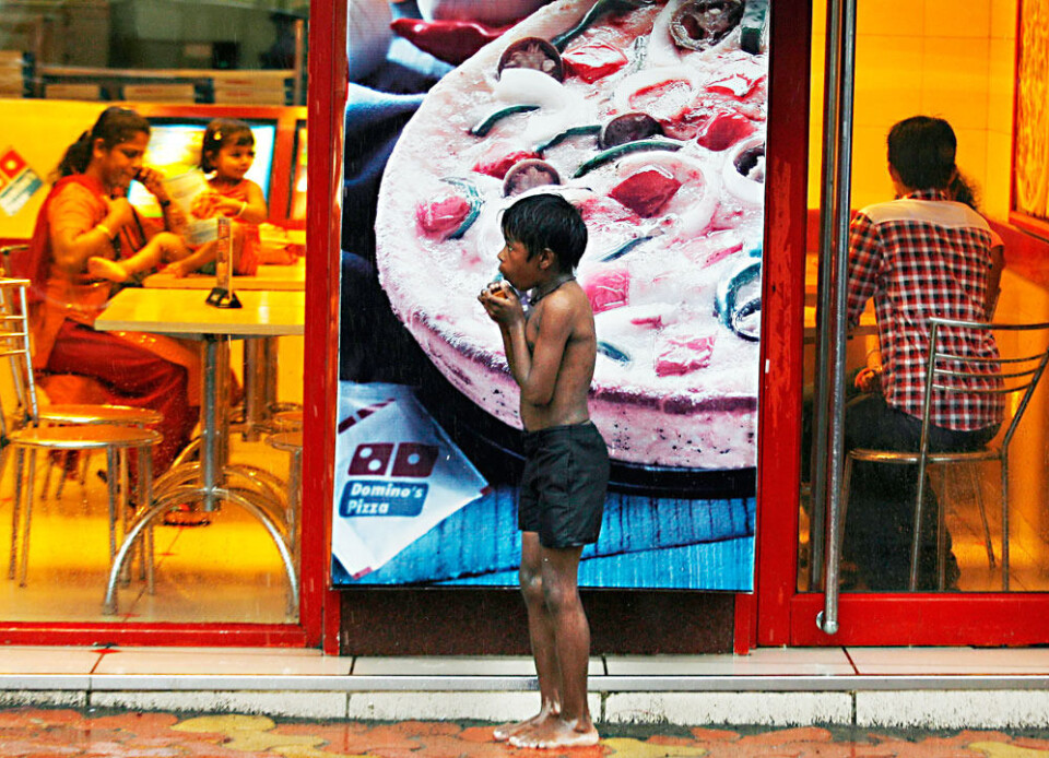 En gategutt søker tilflukt for regnet utenfor en pizzarestaurant i Mumbai. 72 prosent av verdens aller fattigste bor i mellominntektsland. Foto: Scanpix