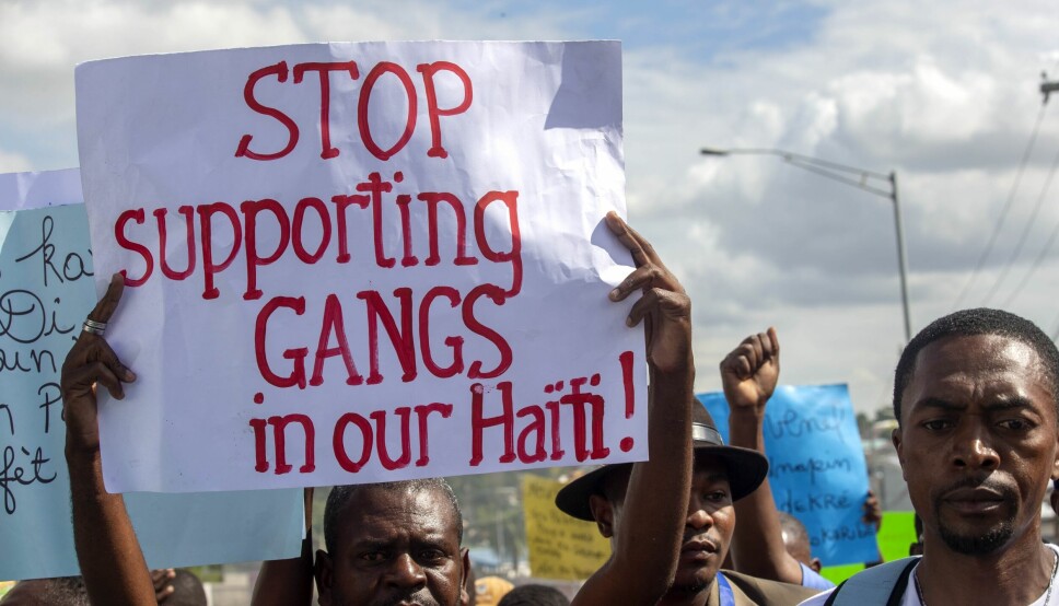 En mann holder opp et skilt med skriften: «Stopp støtten til kriminelle gjenger i vårt Haiti» i en demonstrasjon mot daværende president Jovenel Moise desember 2020.