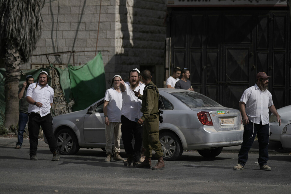 En israelsk soldat snakker med bosettere. I landsbyen Hawara på Vestbredden skal israelske bosettere ha angrepet palestinere torsdag denne uken.