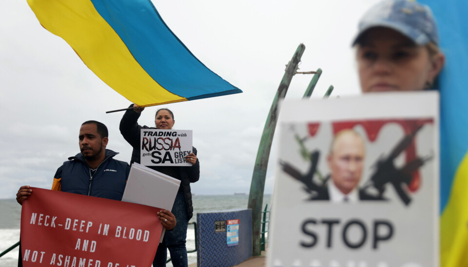 Ukrainere og sørafrikanere demonstrerer mot marineøvelsen som foregår i havområdet i bakgrunnen. Foto: NTB