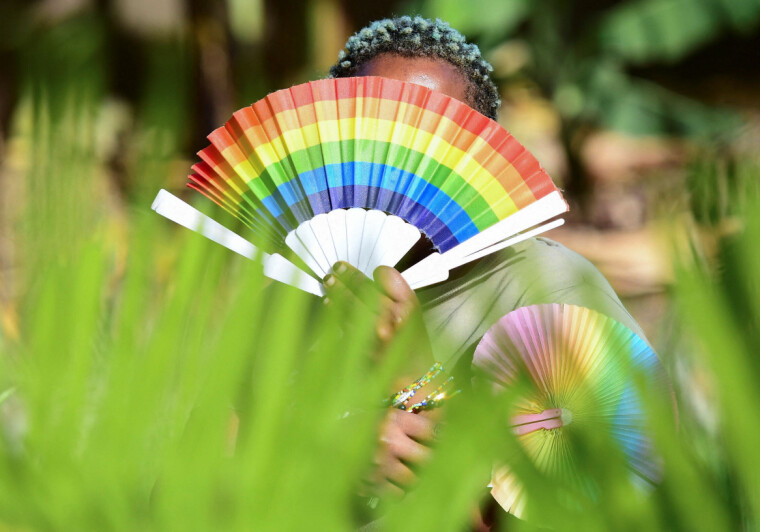 En lhbtiq-person i Kampala, Uganda, dekker ansiktet med en vifte i regnbuens farger i april 2023.