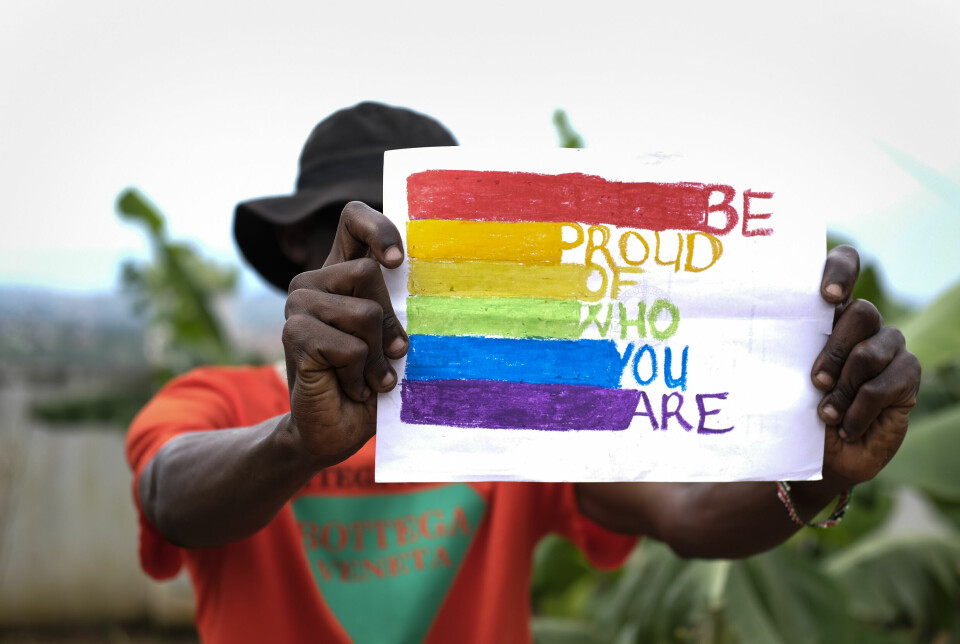 En person dekker ansiktet med en plakat som støtter skeive i Uganda.