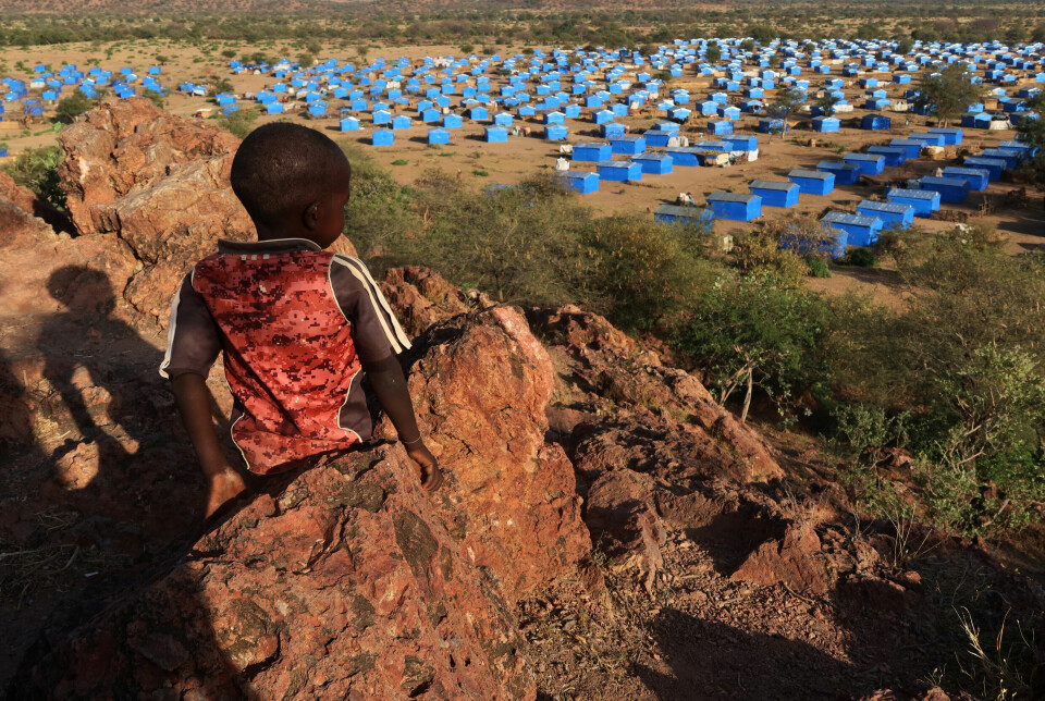 En liten gutt sitter på en høyde ogs ser ut over en flyktningleir ved grensen til Tsjad, vest i landet. Bildet er tatt 9. november 2023.