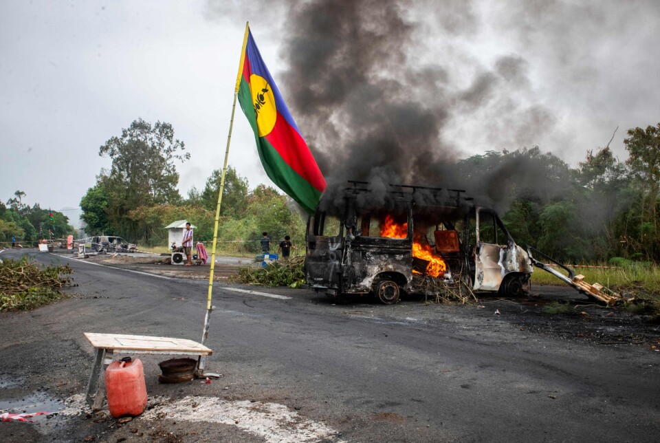 Ny-Kaledonias flagg ved en brennede bil 19. mai. I bakgrunnen en provisorisk veisperring.