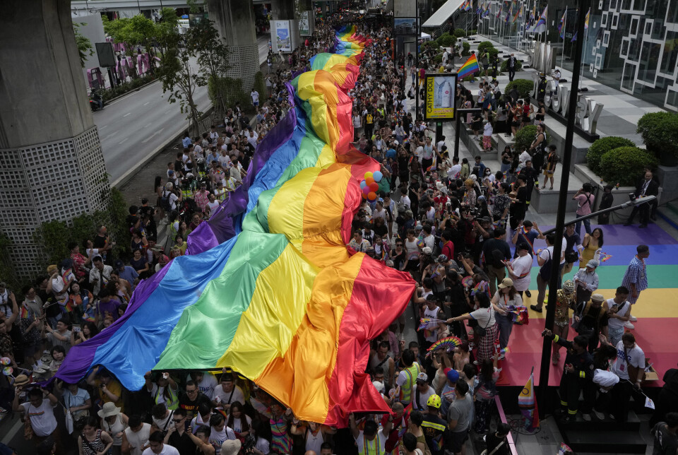 Deltakerne i årets pride-parade i Bangkok holder et stort regnbueflagg over seg mens de går gjennom gatene i byen.