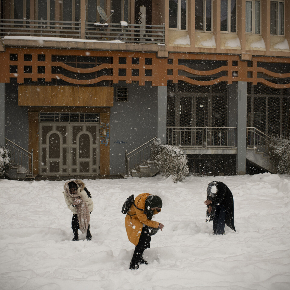Jenter leker i snøen bak en boligblokk et stykke unna hovedveien, skjult fra hovedveien i en forstad til Kabul.
