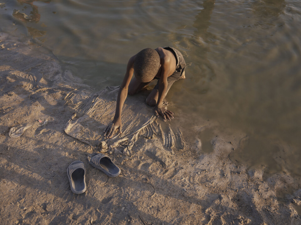En gutt leker i vannkanten i en dam i nærheten av leiren.