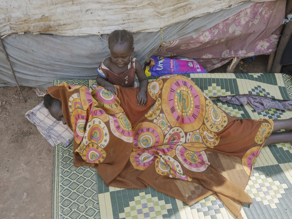 En mor hviler seg i skyggen for den brennhete solen i transittleiren i Renk.