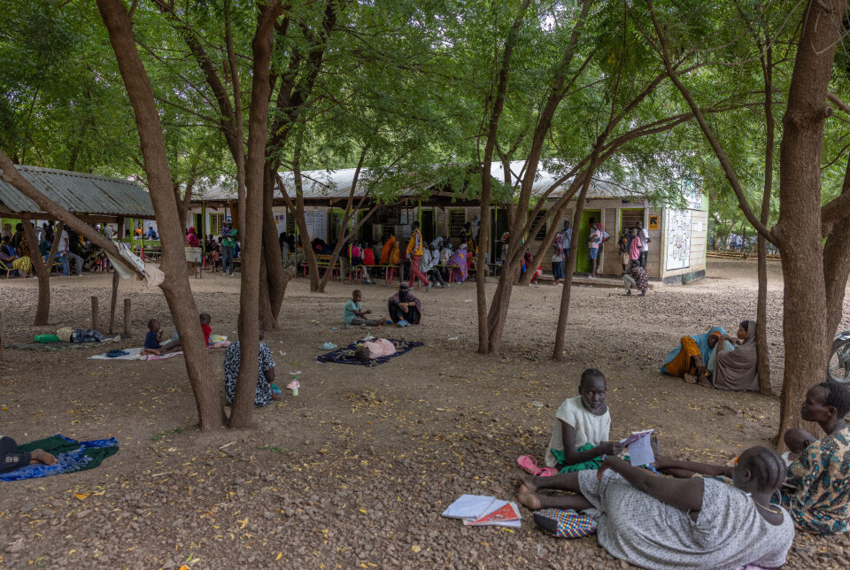 Utenfor helsesenteret Nalemsekon i Kakuma venter pasienter i skyggen av trærne. Det er ikke plass til alle på benkene, og det daglige pasientantallet har økt kraftig etter utbrudd av malaria og kolera. Med store bistandskutt, er ventetiden lang og ressursene knappe.