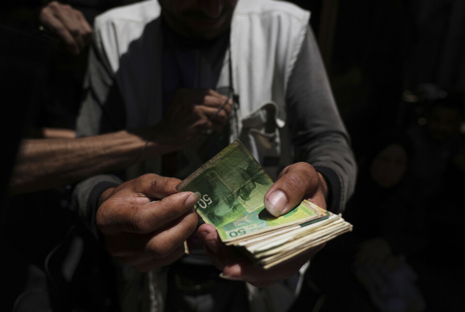 En palestinsk grønnsakshandler viser frem utslitt israelsk valuta i Gaza by. For å kjøpe grønnsaker, mat, vann eller medisiner, må man bruke kontanter.