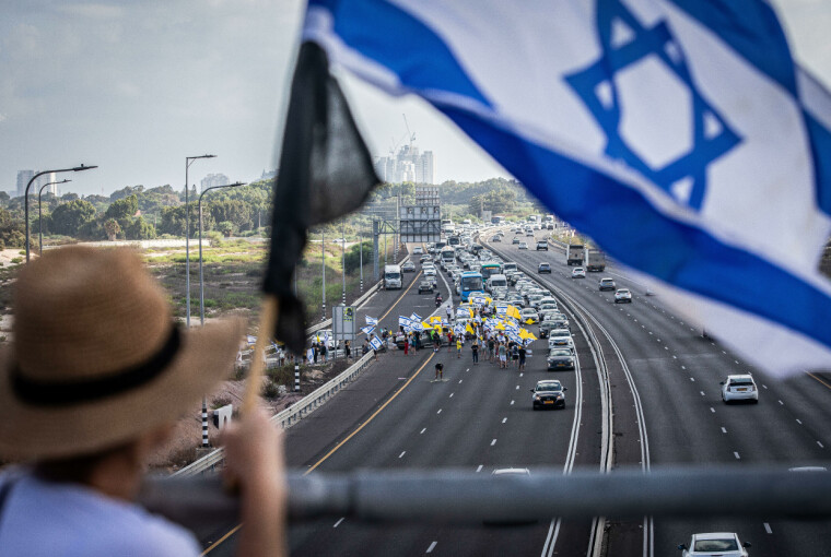 En israelsk kvinne holder landets flagg på en bro over hovedveien i Tel Aviv, som ble blokkert av demonstranter 17. august 2025. Over én million deltok i landsomfattende protester og streik med krav om slutt på Gaza-krigen og løslatelse av de 50 israelske gislene.