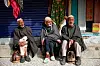 Tre eldre menn sitter foran lukkede butikklemmer i en landsby ved Pahalgam.