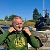 Mann i grønn hettegenser merket «Ukrainian 2SD convoy Norway» foran biler og minnesmerke