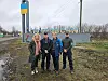 Fire personer står foran et byskilt med ukrainske farger ved en landevei.