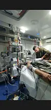 Pasient koblet til overvåkning og utstyr inne i ambulanse mens helsearbeider jobber ved siden av