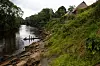 Små båt med personer på en elv ved tett vegetasjon og en bratt, grønn skråning i Amazonas.