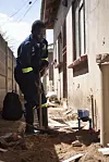 Brannmann bruker et verktøy ved en skadet vegg i et smalt smug.