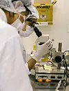To personer i verneutstyr undersøker en prøve i mikroskop på et laboratorium.