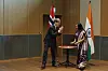 Åsmund Aukrust står ved et bord og signerer en avtale mens en kvinne ser på, med Norges og Indias flagg i bakgrunnen.