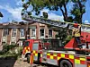 Brannmannskaper på en stigebil ved et skadet tak, med en rød brannbil foran bygningen.