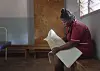Jordmor sitter på en benk og skriver i en stor journalbok ved en helsestasjon.