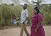 To helsearbeidere går langs en jordvei foran høyt gress i Malawi.