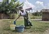 Gravid kvinne bøyer seg for å hente vann fra en bøtte ved et hus på landsbygda i Malawi.
