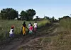 Fire personer går på en gjengrodd jordvei med spor og groper i landskapet i Malawi.