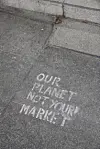 Slagordet «Our planet not your market» er skrevet med kritt på grått fortau.