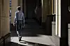 En person går bortover en smal gang mellom bygninger, med sterke lys- og skyggesoner.