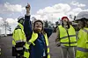 Frøya Skjold Sjursæther står blant flere personer i refleksvester ved vindturbiner og holder en liten vindmølle i plast.
