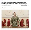 Volodymyr Zelenskyj står i militæruniform foran røde stoler i et lyst rom.