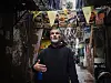 Majdi Majzub står i en trang gate i Shatila-leiren, omgitt av plakater og bannere.