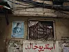 Vegger i en slitt bygning i Shatila med portrett av Yasir Arafat og en innrammet åpning med gitter.