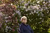 Tore Linné Eriksen sitter foran en blomstrende busk i hagen eller uteområdet ved hjemmet sitt.