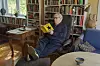 Tore Linné Eriksen sitter i en stol og leser en gul bok i en stue med bokhyller.