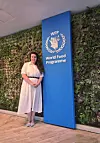 Kvinne står ved et blått skilt med WFP-logo og teksten World Food Programme foran en grønn vegg.