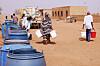 Personer fyller vannkanner ved blå vanntønner ved et gratis utdelingspunkt i Khartoum.