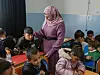 Lærer i rosa hijab underviser barn ved pulter i et klasserom.