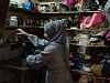 Kvinne i hijab står i et trangt teltkjøkken med hyller fulle av matvarer, servise og klær.