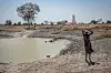 Kvinne bærer vann ved en nesten uttørket dam i et tørt landskap.