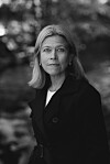 Kvinne i mørk jakke står utendørs foran uskarp bakgrunn.