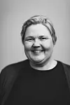 Svart-hvitt-portrett av en smilende kvinne mot lys, nøytral bakgrunn.
