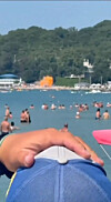 Folk bader i sjøen mens en oransje eksplosjon ses ved strandkanten i bakgrunnen.