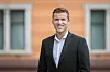 Ung mann står foran en bygning og smiler mot kamera.