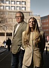 Mann og kvinne i formelle klær står foran kontorbygninger i en by.