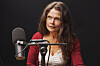 Cecilie Hellestveit sitter ved en mikrofon i et mørkt podcaststudio.