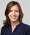 Kvinne med brunt hår og mørk blå bluse poserer mot en lys bakgrunn.